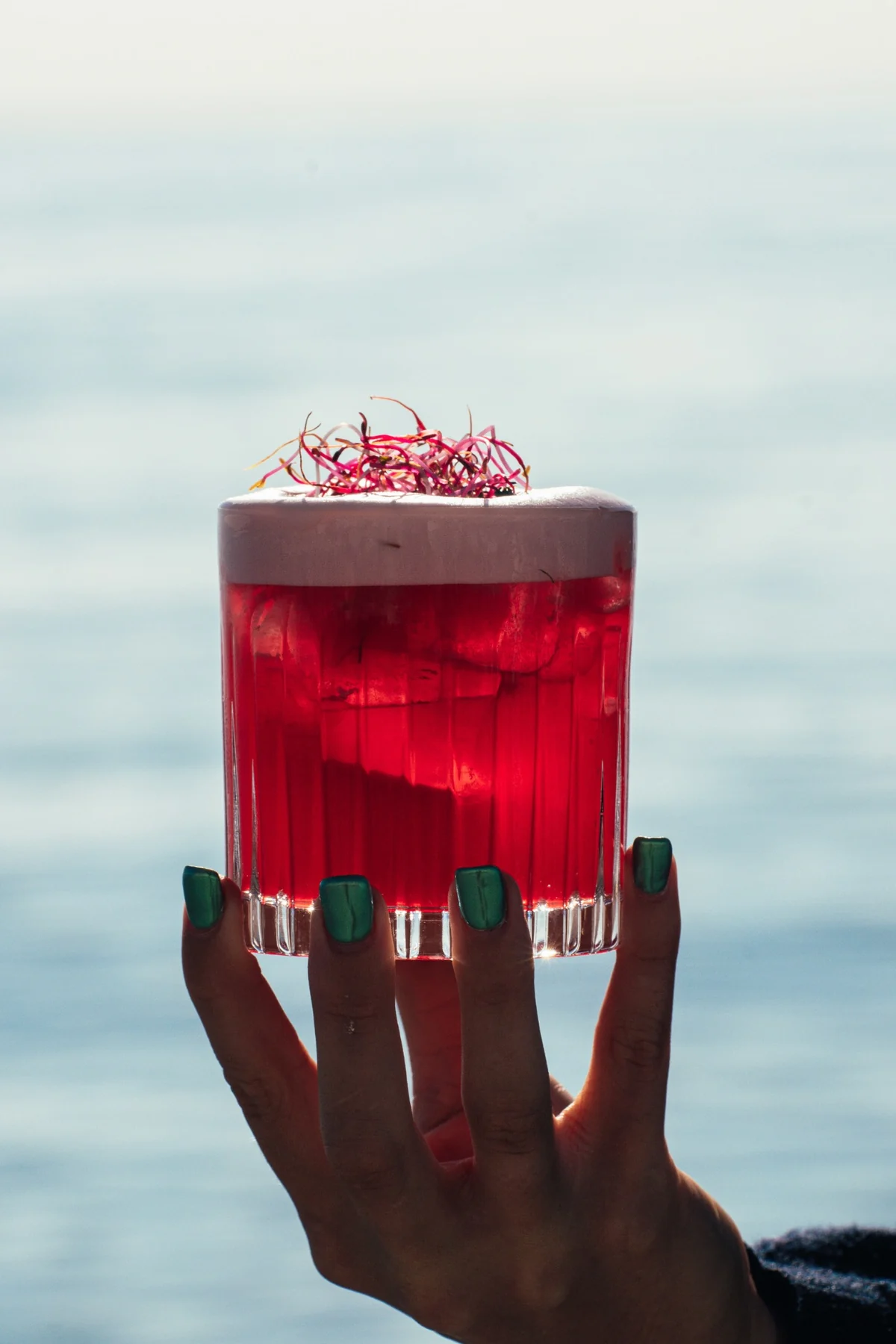 Cocktail rouge tenu à la main face à la mer