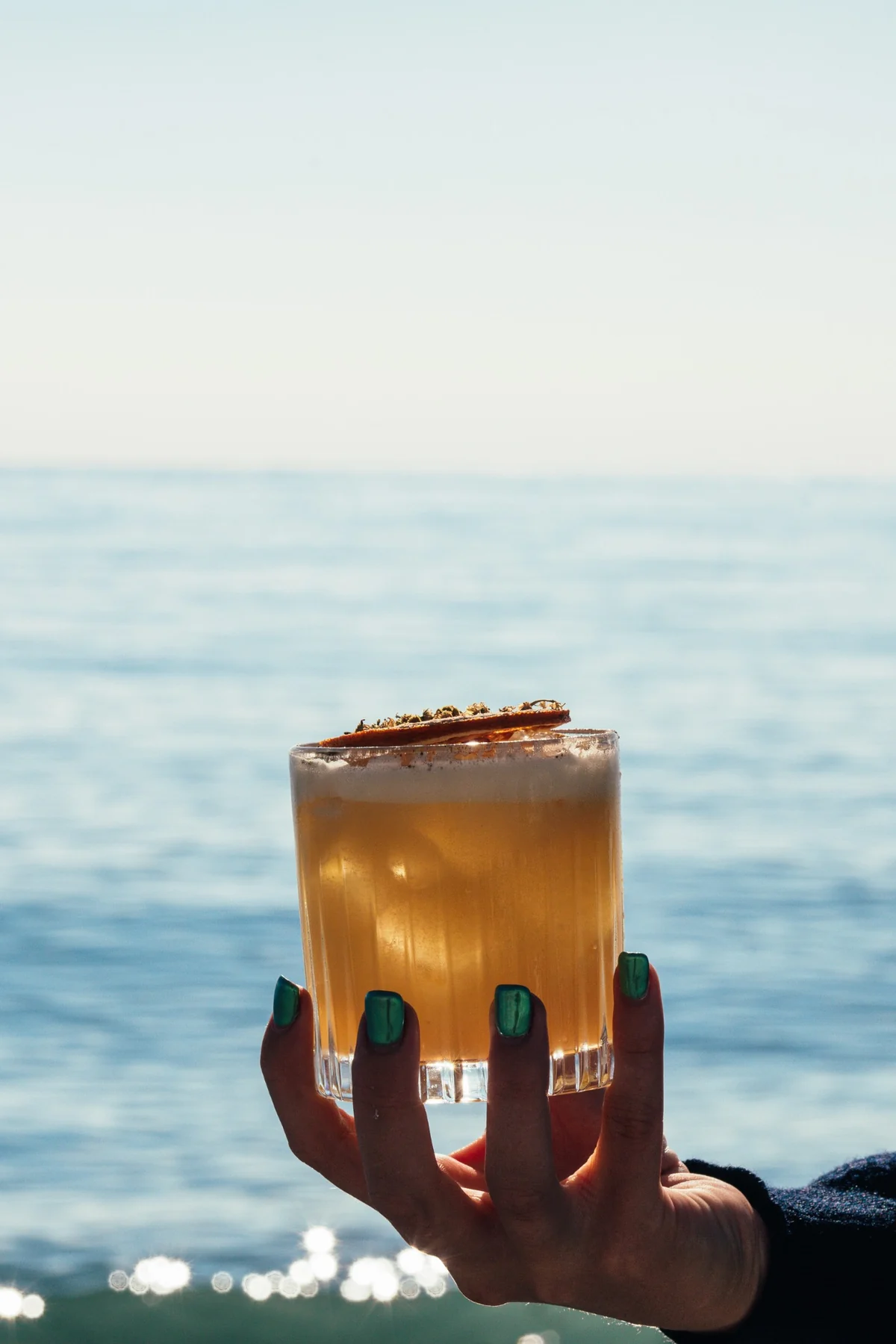 Cocktail doré tenu à la main face à la mer