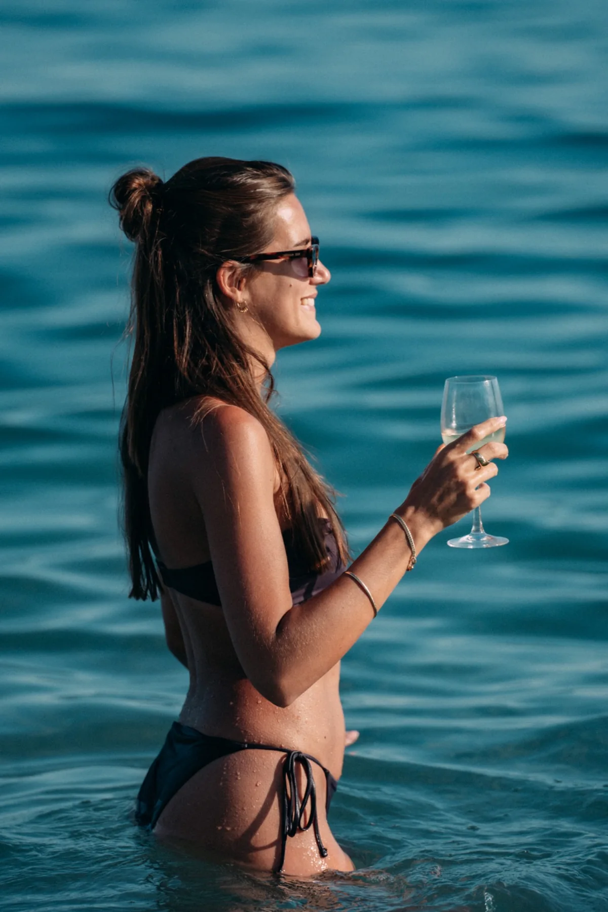 Femme souriante tenant un verre dans la mer
