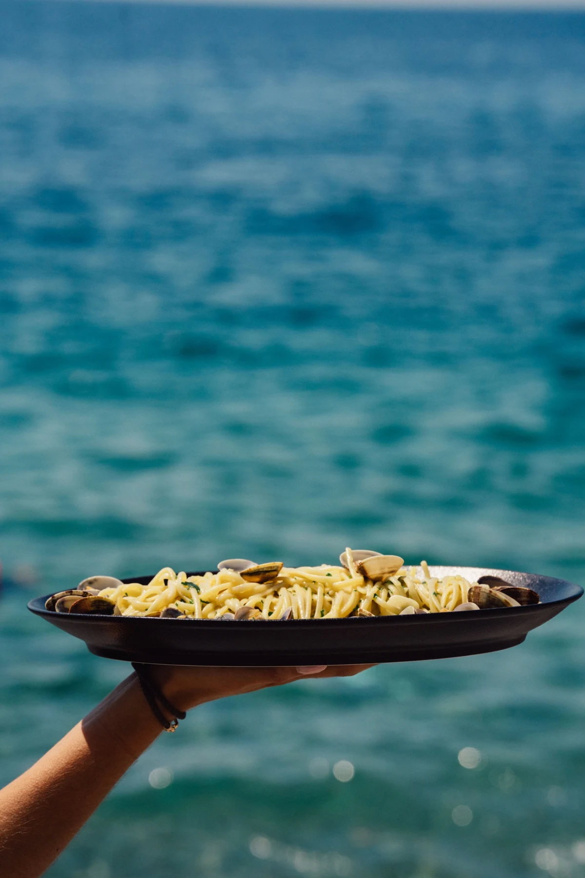 Plat de linguine aux palourdes tenu face à la mer